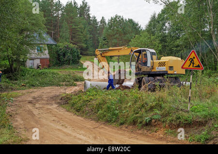 Le constructeur sur l'excavatrice creuse le sable pour le pont - un tuyau à travers un flux. Banque D'Images