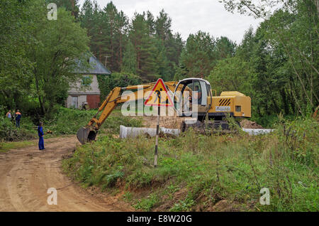 Le constructeur sur l'excavatrice creuse le sable pour le pont - un tuyau à travers un flux. Banque D'Images