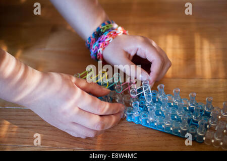 Une petite fille travaille sur le tissage d'un bracelet sur son métier à Arc-en-ciel, un jouet loom utilisée pour tisser des bandes de caoutchouc en bracelets et charms. Banque D'Images