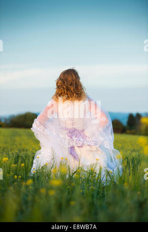 Le Runaway bride - une jeune femme fille dans une robe de mariage l'article en toute confiance dans un champ de fleurs jaunes soir Banque D'Images