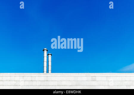 Espace industriel linéaire. Le mur de marbre blanc et deux cheminées industrielles de l'acier contre l'arrière-plan de ciel bleu profond Banque D'Images