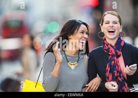 Les femmes rient ensemble walking down city street Banque D'Images