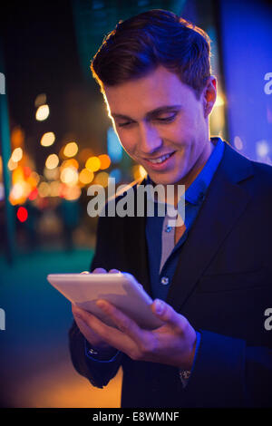 Man using digital tablet on city street at night Banque D'Images