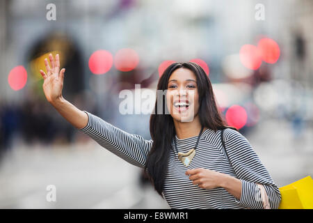 Woman waving pour taxi on city street Banque D'Images