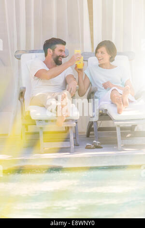 Couple toasting each other dans les chaises de parterre en piscine Banque D'Images