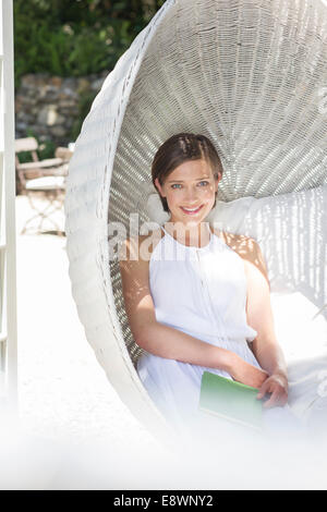 Smiling woman relaxing in hanging wicker chair Banque D'Images