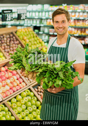 Greffier carrying basket de produire in grocery store Banque D'Images