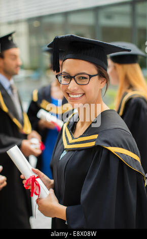 Élève de cap and gown debout avec des amis Banque D'Images