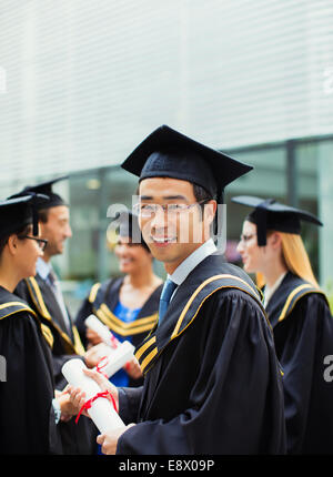 Élève de cap and gown debout avec des amis Banque D'Images