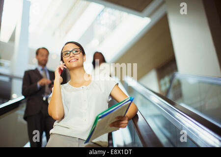 Businesswoman talking on cell phone en descendant l'escalator Banque D'Images