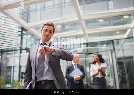 Businessman looking at watch walking out of office building Banque D'Images