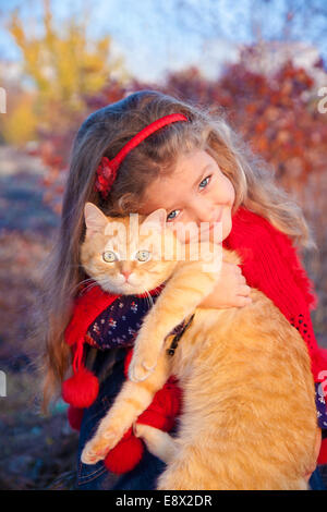 Petite fille tenant un chat rouge en automne Banque D'Images