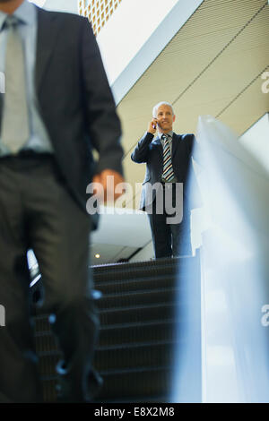 Businessman talking on cell phone en haut de l'escalator in office Banque D'Images