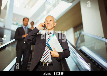 Businessman talking on cell phone going down escalator Banque D'Images