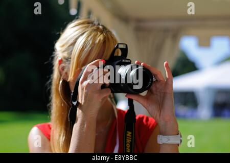 Une femme à une garden party nous tend un appareil photo Nikon, concentrant l'objectif avec sa main gauche Banque D'Images