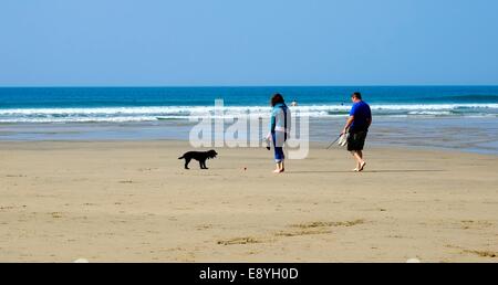 Un couple avec un chien noir à jouer au ballon sur la plage Cornwall England uk Rolvenden Banque D'Images