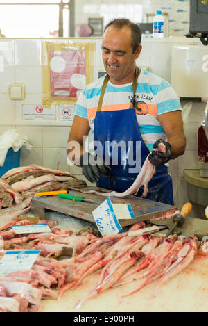 Portugal Algarve Olhao port market town homme chauve tablier bleu gants noirs l'éviscération du poisson rose rouge préparation de nettoyage à vendre Banque D'Images