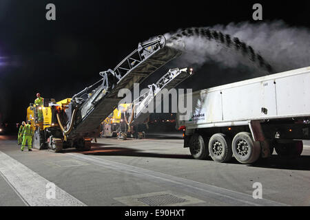 Les équipes d'entretien refaire une piste de l'aéroport au cours d'une fermeture du jour au lendemain. Deux avions de la route à l'écart de la surface supérieure. Banque D'Images