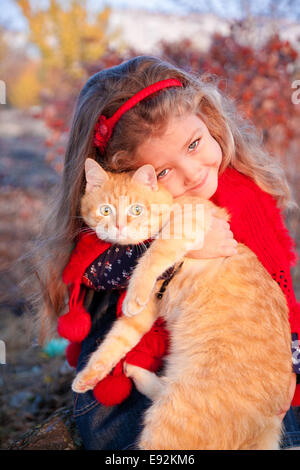 Petite fille tenant un chat rouge en automne Banque D'Images