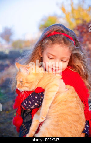 Petite fille tenant un chat rouge en automne Banque D'Images