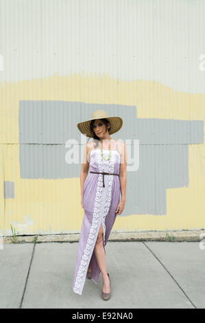 Jeune femme en robe violette longue avec fente et Grand Brim Hat contre mur peint Banque D'Images