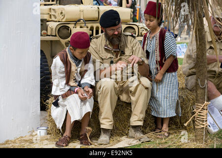 Soldat faisant une poupée en roseau avec des enfants habillés traditionnellement Sur le campement des rats du désert à Kandahar Banque D'Images