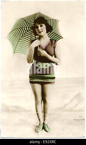 Femme en maillot rayé marron et vert, parasol à rayures Service Standing on Beach, Hand-Colored, carte postale, vers 1900 Banque D'Images