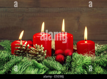 La décoration de l'avent festive avec quatre boules rouge brûler des bougies, et des branches d'arbre de Noël en arrière-plan des vacances. Banque D'Images