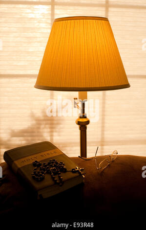 Bible sur l'arrière de la table avec la lumière solaire et la lumière chaude de la lampe avec rosaire et verres Banque D'Images