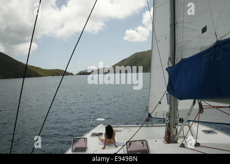 Une jeune femme est assise sur le pont d'un grand voile en vacances dans le BVI. Banque D'Images