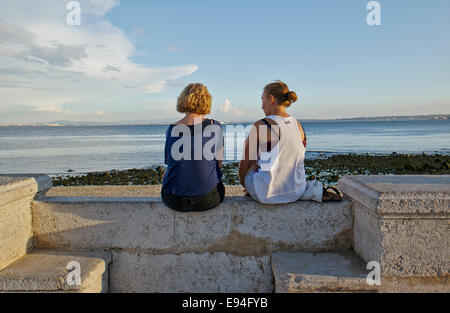 Deux jeunes femmes assises à Praça do Comércio au cours de soir en contemplant l'océan Atlantique, la Baixa Pombalina, à Lisbonne, Portugal Banque D'Images