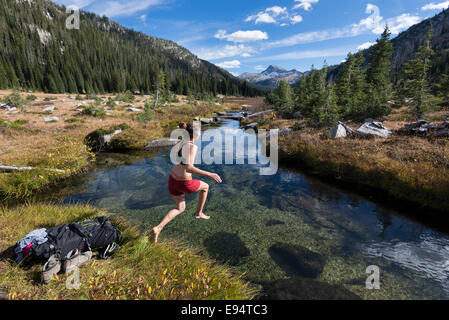 Femme sautant dans un ruisseau sur un sac à dos voyage en Oregon's Montagnes Wallowa. Banque D'Images