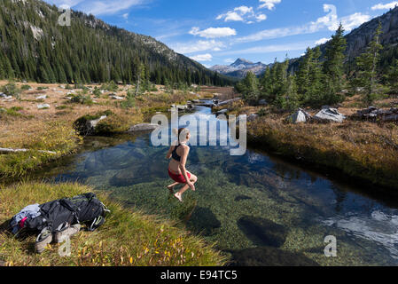 Femme sautant dans un ruisseau sur un sac à dos voyage en Oregon's Montagnes Wallowa. Banque D'Images