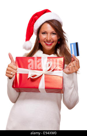 Smiling woman wearing a Santa hat rouge l'achat de cadeaux de Noël sur une carte bancaire brandissant une giftwrapped fort rouge coloré avec un Banque D'Images