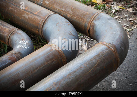 Coude de pipeline en acier industriel sur l'asphalte de la route en milieu urbain Banque D'Images