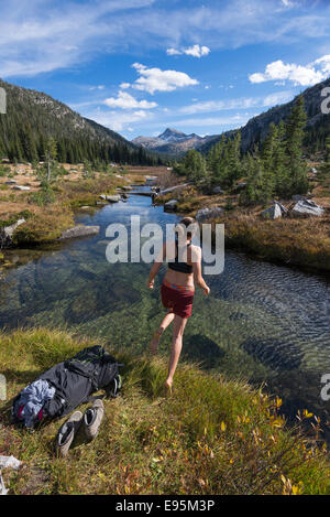 Femme sautant dans un ruisseau sur un sac à dos voyage en Oregon's Montagnes Wallowa. Banque D'Images