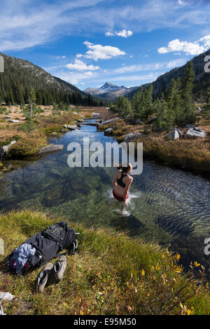 Femme sautant dans un ruisseau sur un sac à dos voyage en Oregon's Montagnes Wallowa. Banque D'Images