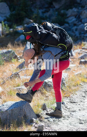 Femme attachant ses lacets sur un sac à dos voyage en Oregon's Montagnes Wallowa. Banque D'Images