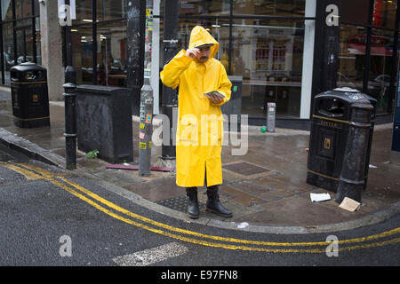 Un homme portant un manteau imperméable jaune donne des dépliants sur Brick Lane dans l'Est de Londres, au Royaume-Uni. Banque D'Images