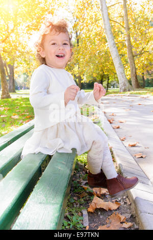 Heureuse petite fille assise sur un banc dans le parc Banque D'Images