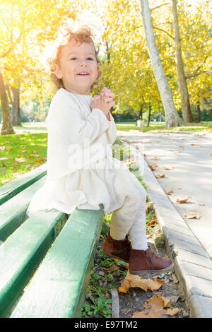 Heureuse petite fille assise sur un banc dans le parc Banque D'Images