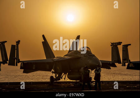 L'US Navy UN F/A-18E Super Hornet est découpé par le coucher de soleil sur le pont d'envol du porte-avions USS Carl Vinson lors des opérations contre l'Etat islamique le 16 octobre 2014 dans la mer d'Oman. , Alors que le navire prend en charge la résolution inhérente. Le président Barack Obama a autorisé l'acheminement de l'aide humanitaire à l'Iraq, ainsi que des frappes aériennes ciblées pour protéger le personnel américain de la part des extrémistes connus sous le nom de l'État islamique en Irak et au Levant. Le Commandement central américain dirigé les opérations. Banque D'Images