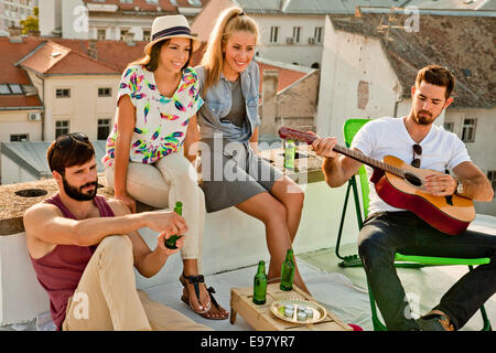 Les jeunes à l'écoute de guitariste at rooftop party Banque D'Images