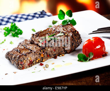 Servant de filet de boeuf grillé enrobé de poivre chaud et garni de fines herbes et une tomate Banque D'Images