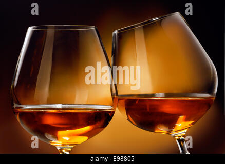 Pour clink deux verres de Cognac ou Brandy liqueur en face d'un fond brun. Banque D'Images