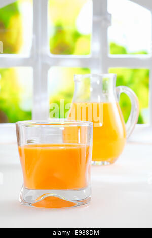 Jus d'orange fraîchement pressé en bonne santé dans un verre Tumbler avec une verseuse en verre rempli de jus de fruits, debout devant une nouvelle fenêtre d'été. Banque D'Images