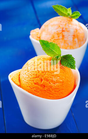 Libre d'un cycle de boule de crème glace coloré orange garnie de Mint en porcelaine en forme de bateau, bols sur blue boards Banque D'Images