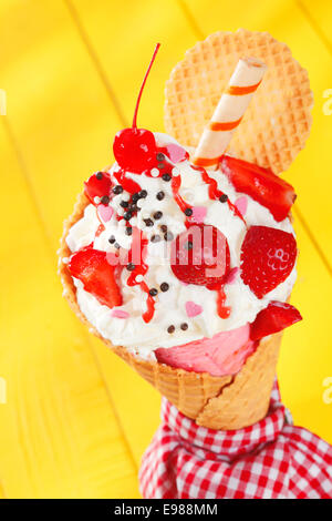 Partie colorée de cornets pour crème glacée glace garnie de fraises rouges bien mûrs et une spirale sur un biscuit gaufrette cheerful fond jaune Banque D'Images