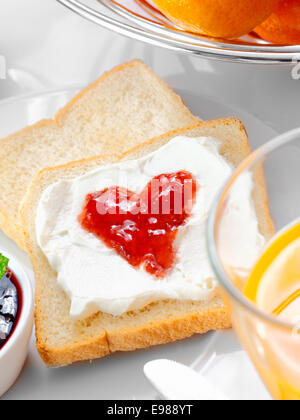 Confiture de fraise en forme de cœur sur la garniture de crème fouettée d'épaisseur d'une tranche de pain blanc frais Banque D'Images