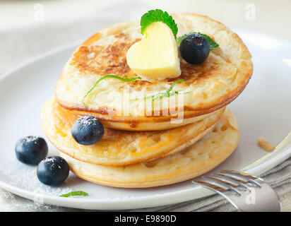 Pile de des blinis ou pancakes d'or surmontée d'un pat en forme de coeur de beurre et servi avec des bleuets frais Banque D'Images